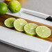 A cutting board with limes and a knife on a counter.
