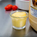 A small glass cup with yellow liquid in it next to a jar of Ken's Foods Golden Honey Mustard Dressing.