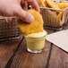 A hand dipping chicken into a small bowl of Ken's Golden Honey Mustard Dressing.