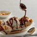 A bowl of ice cream with chocolate syrup, a banana, and a spoon.
