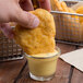 A hand holding a piece of fried fish dipping into Ken's Dijon Honey Mustard Dressing in a small glass cup.