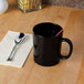 A black mug with a straw on a wooden table.