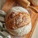 A loaf of bread on a cutting board with a bowl of King Arthur Organic Bread Flour.