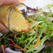 A hand pouring Gulden's Spicy Brown Mustard over a salad.