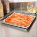 A pizza on an American Metalcraft Hard Coat Aluminum square pizza pan on a counter.