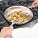 A person cooking potatoes in a Vollrath stainless steel frying pan.