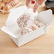 A hand holding a pair of doughnuts in a white Fold-Pak paper take-out box.