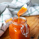 A spoon pouring orange sauce into a jar of Sweet Baby Ray's Mango Habanero Wing Sauce and Glaze.