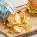 A bag of Dirty Potato Chips Cracked Pepper and Sea Salt next to a burger on a cutting board.
