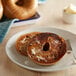 A white plate with a New York Style Cinnamon Raisin Bagel with butter and a knife.
