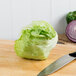 A lettuce head on a cutting board next to a knife.