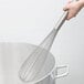 A hand holding a Carlisle stainless steel French whisk over a large pot.