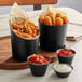 Three black Acopa stainless steel containers filled with French fries and dipping sauces.