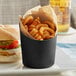 A matte black stainless steel cup filled with French fries and a burger.