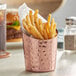 An Acopa hammered copper French fry cup filled with fries on a table in a restaurant.