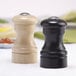 A Chef Specialties ebony pepper shaker and natural salt shaker set on a table.