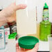 A hand holding a Carlisle white plastic container with a green lid and spout.