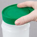 A hand holding a Carlisle white plastic container with a green lid.