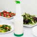 A white Carlisle Store 'N Pour container with green spout and cap on a table with salad.