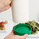 A hand using a green spout to pour white liquid into a Carlisle white container with a green cap.