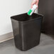 A hand spraying a white Rubbermaid medical wastebasket with a green and white can.