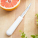 A Dexter Russell grapefruit knife next to a half of a grapefruit on a cutting board.