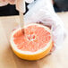 A person's hand using a Dexter Russell grapefruit knife to cut a grapefruit.
