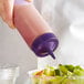 A hand pouring purple liquid from a Vollrath Color-Mate Squeeze Bottle into a salad.