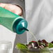 A hand using a Vollrath green wide mouth squeeze bottle to pour dressing onto a salad.