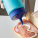A hand using a Vollrath blue wide mouth squeeze bottle to put mayo on a sandwich.