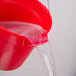 A red Rubbermaid BRUTE bucket pouring water into a sink.