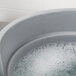 A Rubbermaid gray round bucket filled with soapy water over a sink.