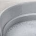 A Rubbermaid gray round bucket filled with soapy water and bubbles.