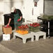 A man in a green apron putting tomatoes in a plastic container on a Cambro bow tie dunnage rack.