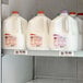 A white Avantco shelf tag holder on a shelf holding jugs of milk.