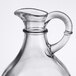 A clear glass Tablecraft olive oil jug with a handle.