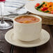 A white Oneida Odyssey bouillon cup filled with red soup on a table with a plate of salad.