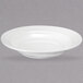 A Oneida Espree cream white china rim deep soup bowl on a grey surface.