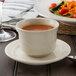 A Oneida cream white china bouillon cup on a saucer with a plate of salad.