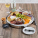 A Frilich stainless steel cooling plate set with cheese, crackers, grapes, and wine on a table.