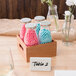 Acopa reusable glass milk bottles with lids in wooden crates on a table with pink and blue balls in jars.