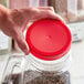 A person's hand holding a 110/400 red plastic lid on top of a jar.