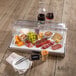 A Frilich clear plastic roll top dome cover on a tray of food and wine on a table.