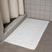 An Oxford Vicenza Bianco white bath mat with a dobby border on a tile floor.