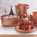 A copper hammered aluminum American Metalcraft beverage tub filled with ice and bottles of wine.
