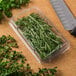 A plastic container of fresh herbs next to a knife on a counter.