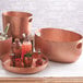 An American Metalcraft copper hammered aluminum round serving tray with copper utensils and fruits on it.