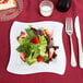 A Fineline white plastic square plate with a salad and strawberries on it.