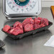 A black CKF foam meat tray on a counter full of raw meat.