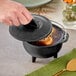 A hand holding a Lodge mini cast iron country kettle lid over a pot of soup.